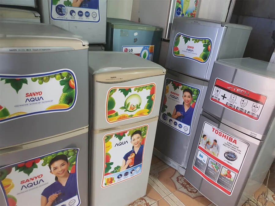 Tủ lạnh Sanyo cũ màu trắng đang mở cửa, bên trong có nhiều ngăn kệ chứa thực phẩm tươi ngon, minh họa kinh nghiệm kiểm tra khi mua.